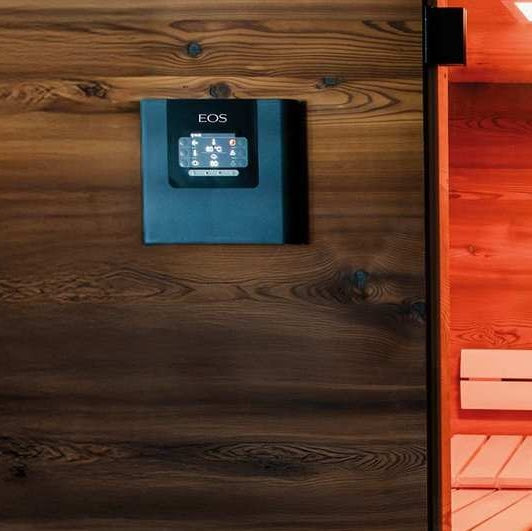 A dark wood sauna interior with a black electronic control panel mounted on the wall, showing the EOS brand name above a small illuminated display.